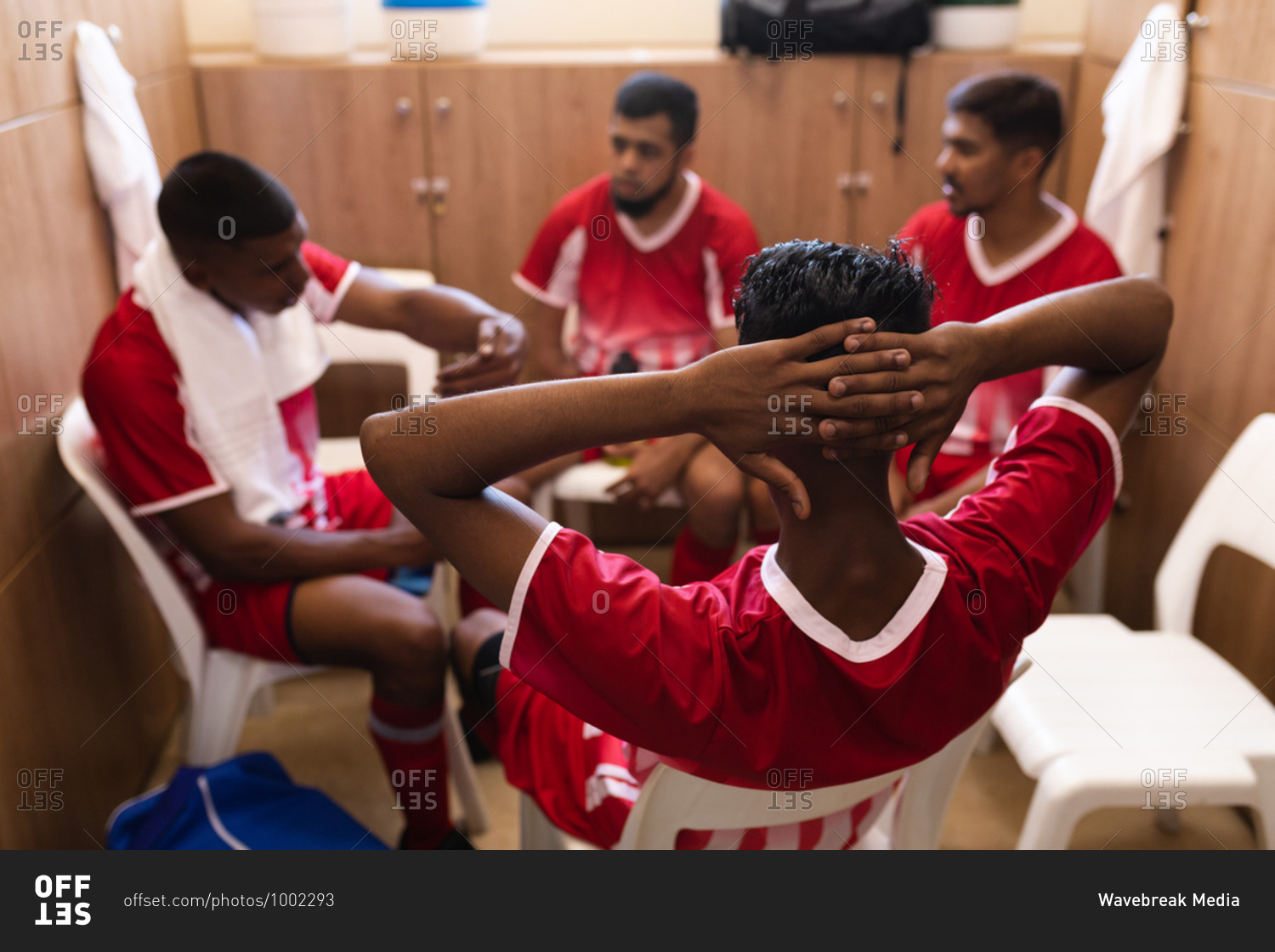 Multi ethnic group of male football players wearing a team strip sitting in changing room during a break in game, interacting and talking.