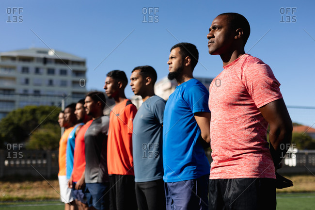 Multi ethnic group of male five a side football players wearing sports clothes training at a sports field in the sun, standing in a row before a game.
