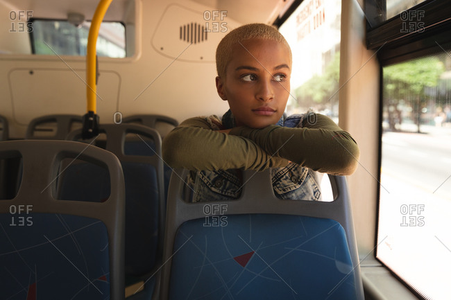 Mixed race alternative woman with short blonde hair out and about in the city, sitting on a bus, leaning on the seat in front, looking out of the window. Independent urban nomad on the go.