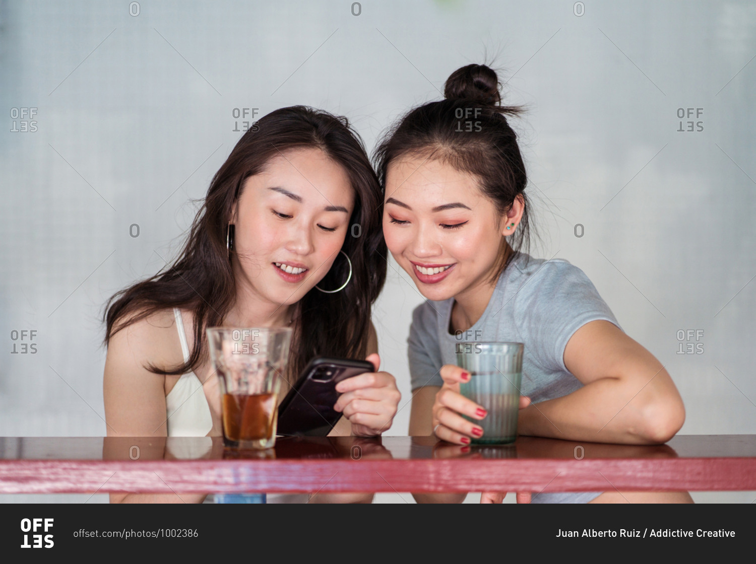 Cheerful ethnic female friends sitting at counter in cafe and browsing cellphone together while relaxing during weekend