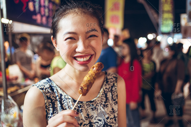 Asian female standing in Zhubei Night Market and cooling hot sausage on stick