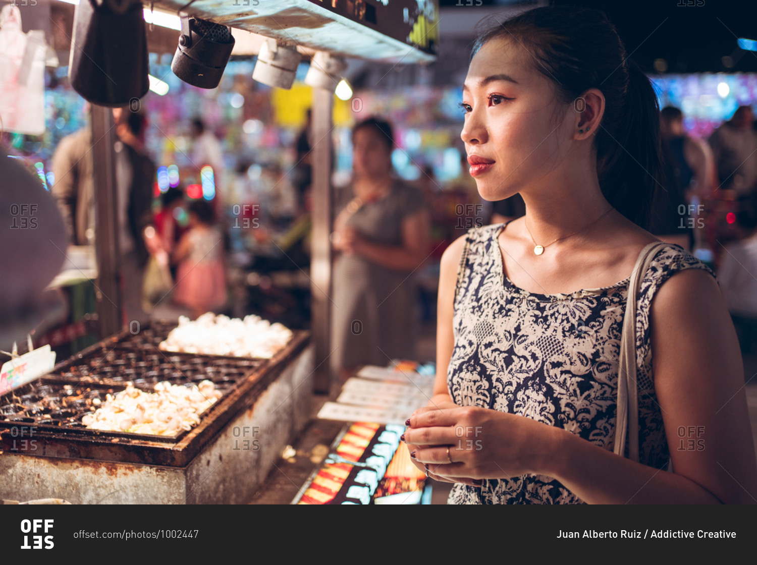 Side view of female in summer dress standing near counter on crowded street in Night Market in Taiwan