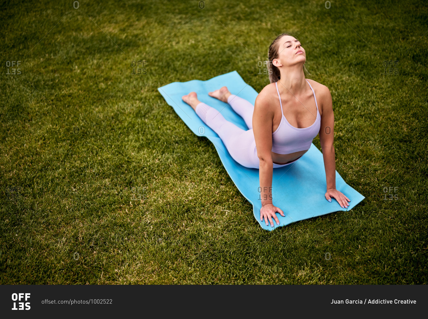 From above side view of peaceful female practicing yoga on mat in Bhujangasana with closed eyes on lawn in backyard