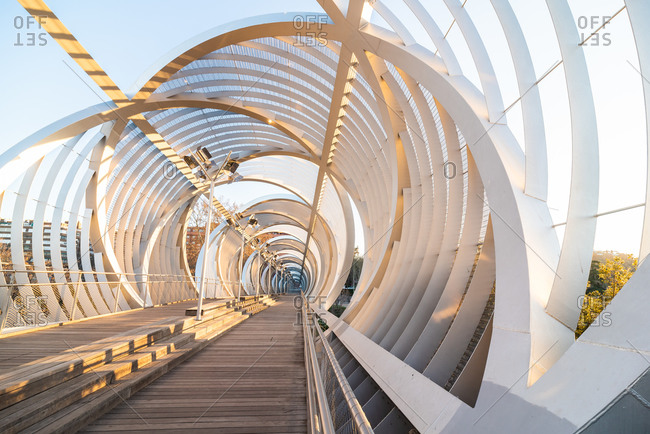 Perspective inside passage of helical cone shaped Arganzuela bridge with internal metal intertwined spirals crossing diagonally in sunset time in Madrid