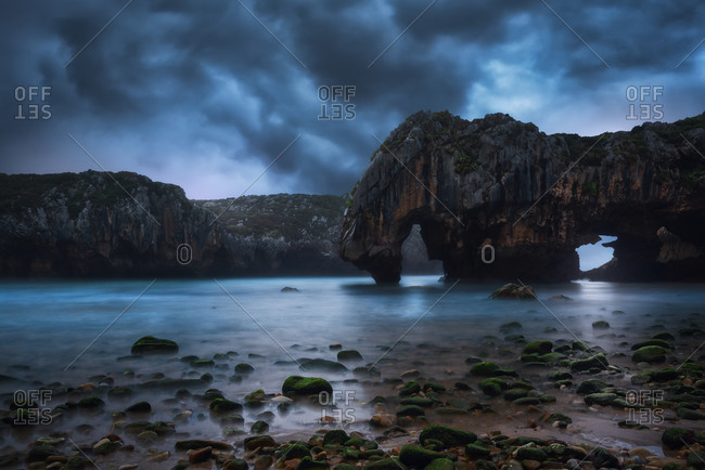 Amazing scenery of sea coast with calm water and rocky cliffs with caves under dark sky with Milky Way