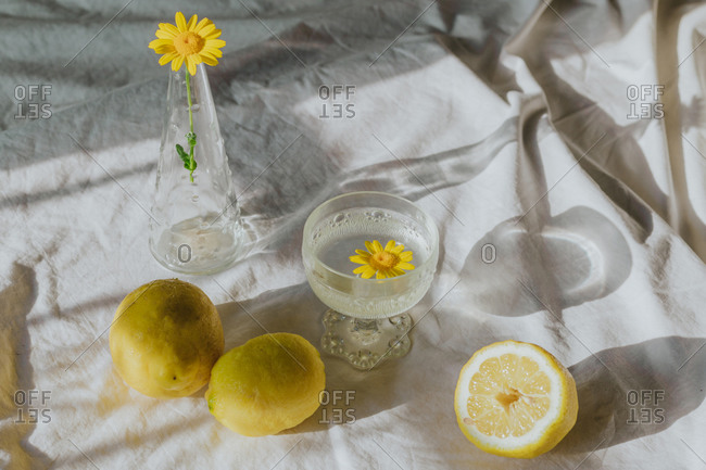 Delicate yellow chamomile in glass vase placed on table with white cloth near refreshing drink and composed with natural lemons