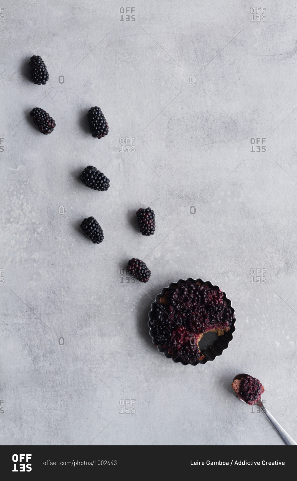 Top view of palatable pie with blackberry arranged in line on table close to spoon