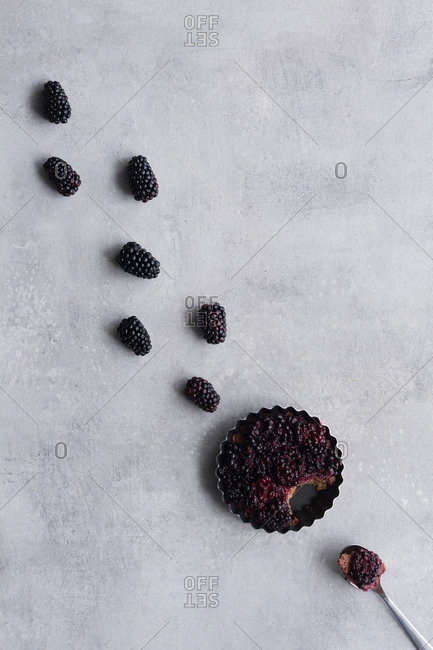 Top view of palatable pie with blackberry arranged in line on table close to spoon