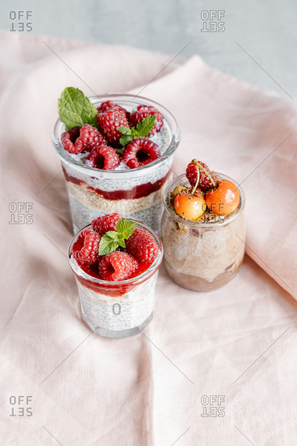 Composition of delicious puddings made from chia seeds yogurt topped with raspberry jam and cherry in glass jars on grey table