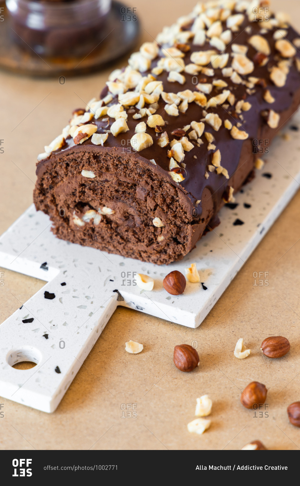 Delicious homemade roll cake with chocolate glaze and hazelnut placed on chopping board in modern kitchen