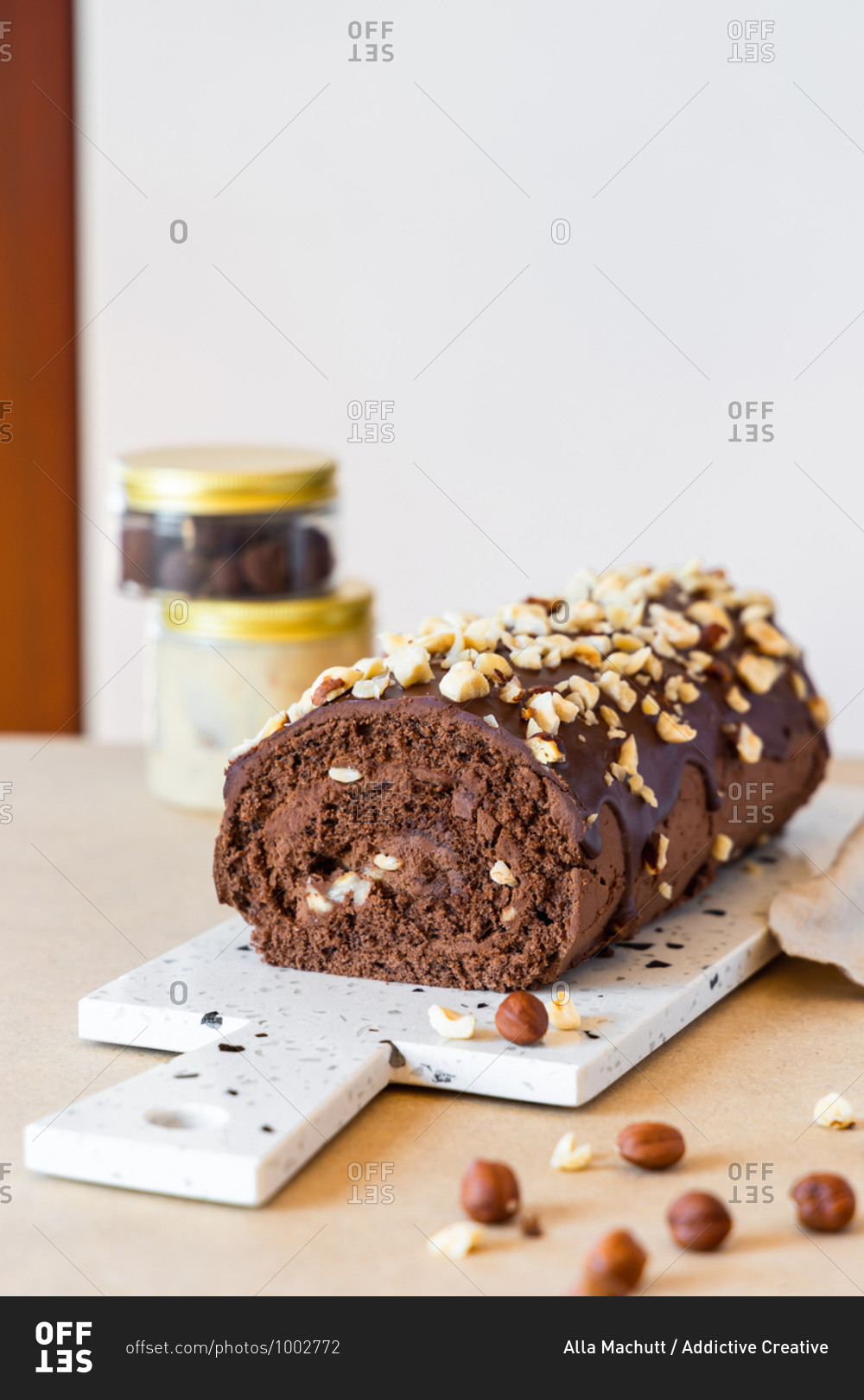 Delicious homemade roll cake with chocolate glaze and hazelnut placed on chopping board in modern kitchen