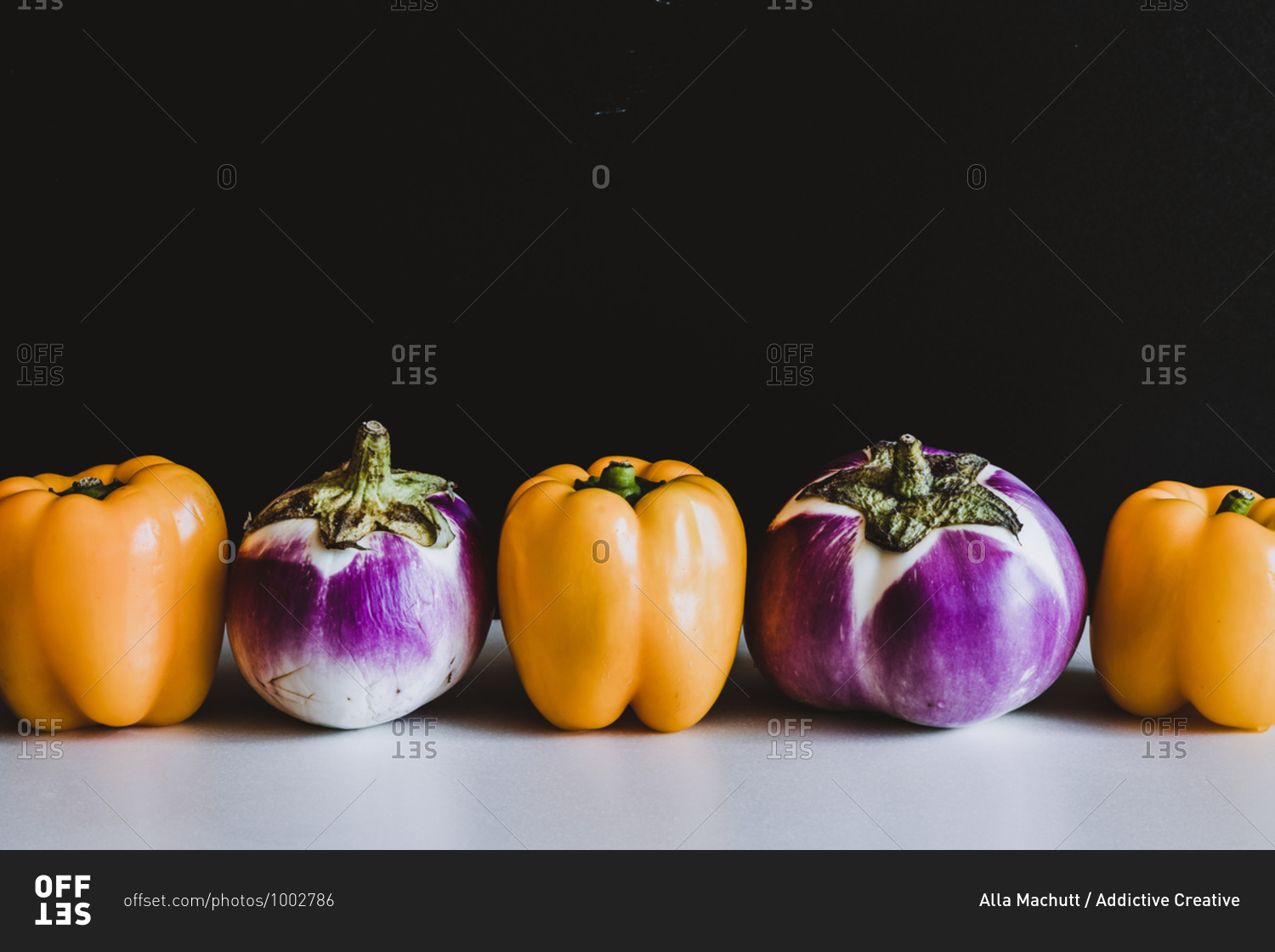 Fresh yellow peppers and eggplants placed in line on table on black background in studio