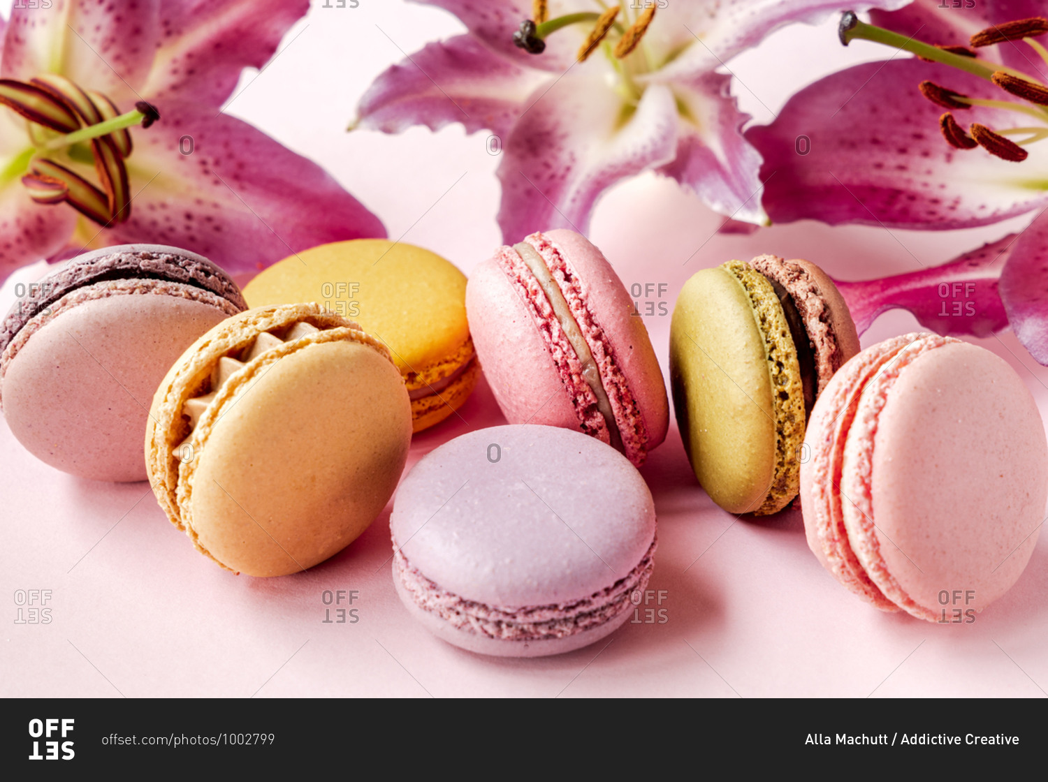 Closeup of assorted delectable macarons placed on pink table with fresh lily flowers