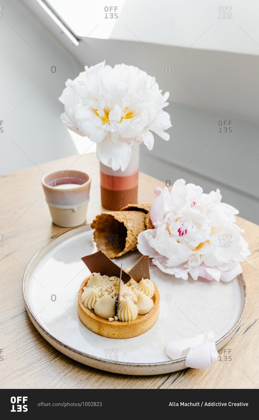 High angle of palatable caramel tart garnished with white and milk chocolate and placed on tray with waffle cones and peony flowers