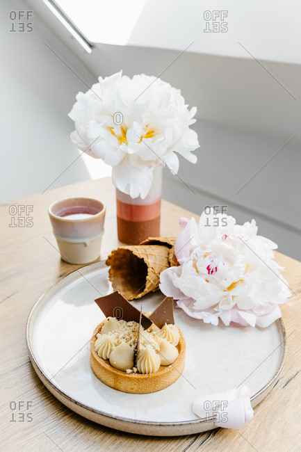 High angle of palatable caramel tart garnished with white and milk chocolate and placed on tray with waffle cones and peony flowers