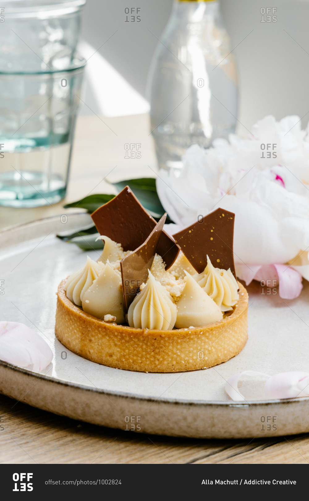 High angle of palatable caramel tart garnished with white and milk chocolate and placed on tray with peony flowers