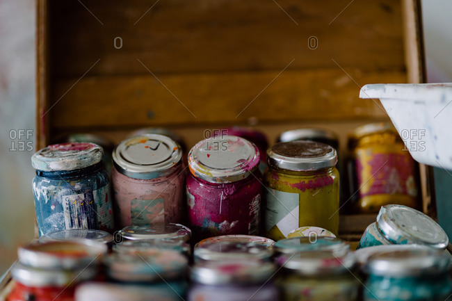 Plastic bottles with colorful paints and empty containers near artist tools on dirty table near multicolored wall with uneven surface in art studio