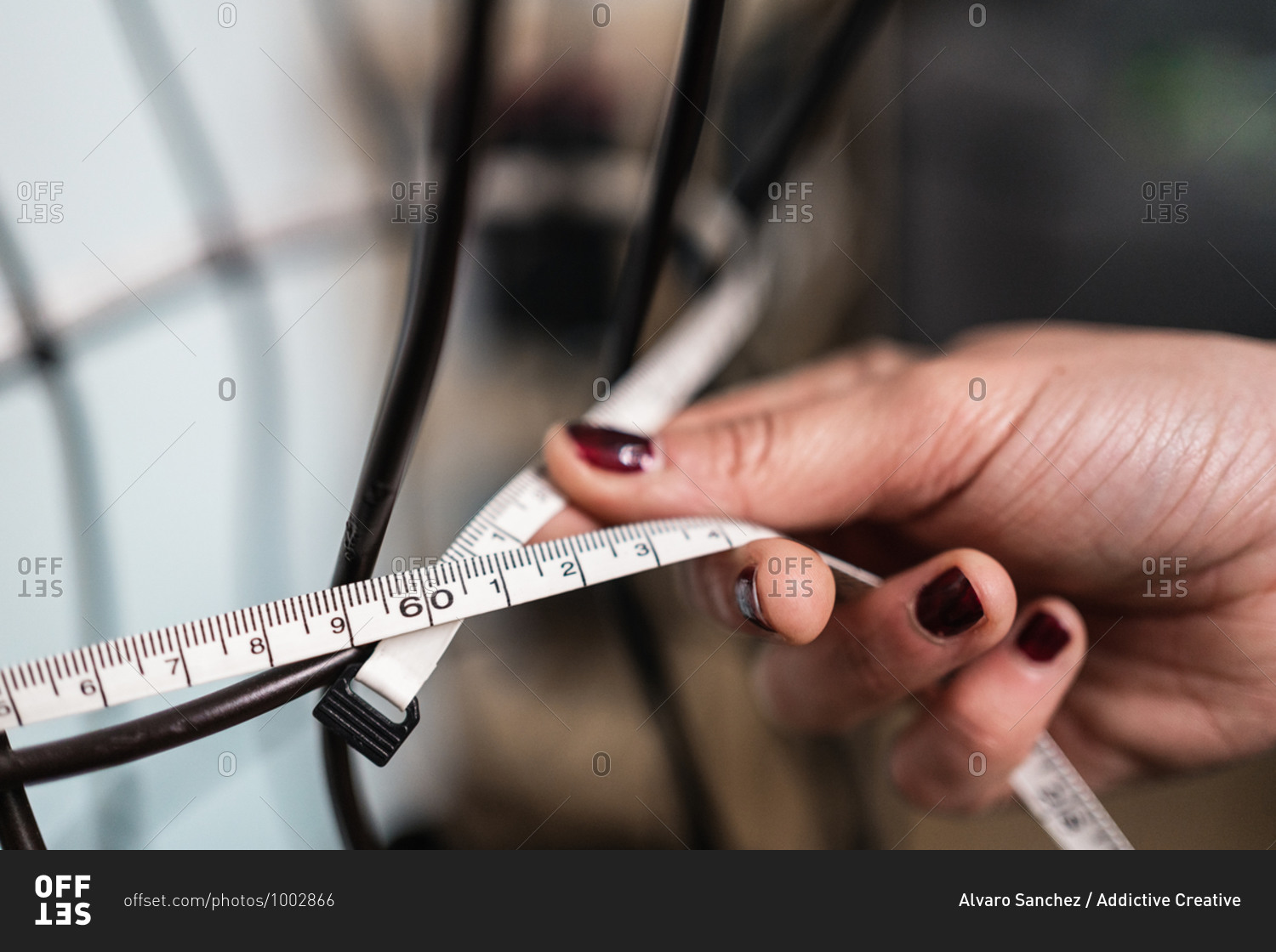 Cropped unrecognizable seamstress taking measurements of wire dummy standing in loft style studio