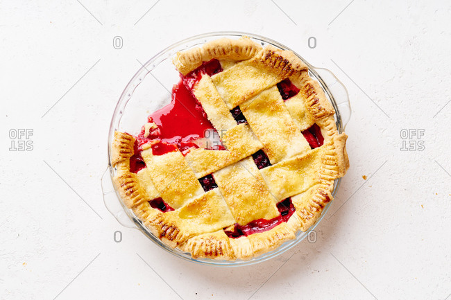 Sweet pie with apples and cranberries decorated with lattice with one slice cut.
