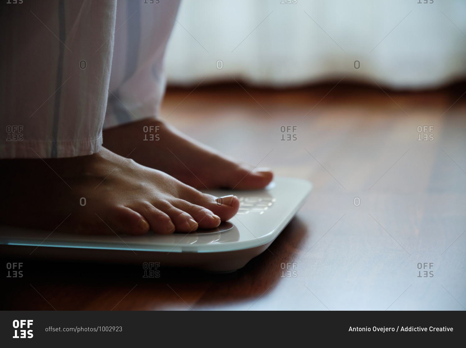 Crop faceless barefoot female in cozy pajama standing on digital weight and body fat scales with display showing healthy weight of 60 kg on bathroom floor in morning