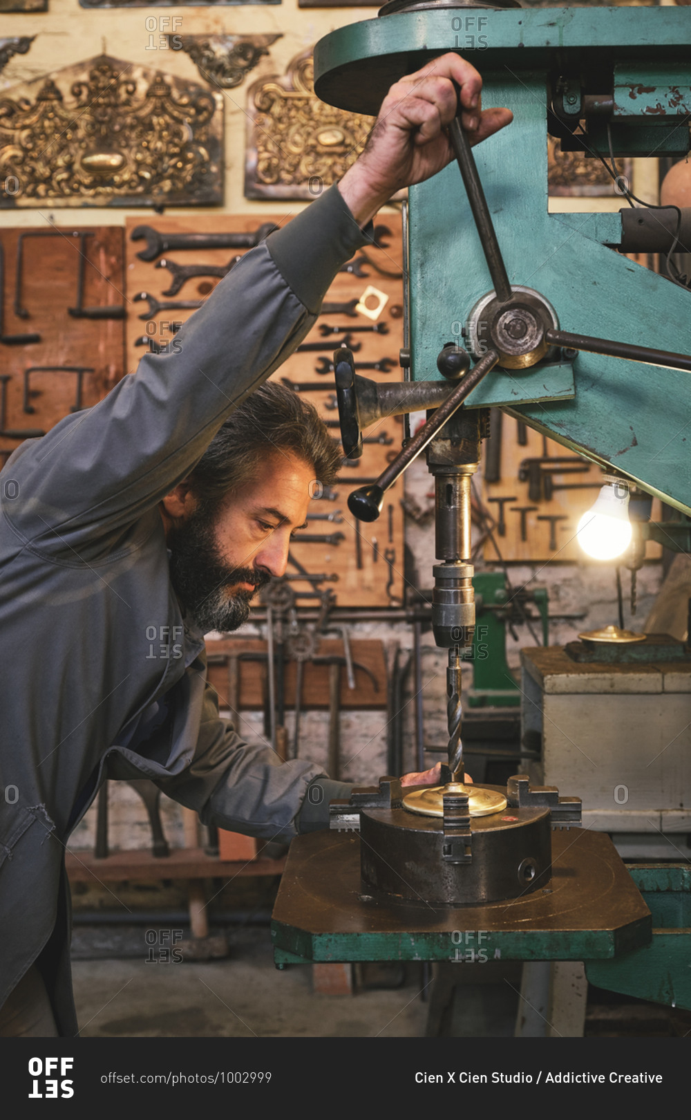 Side view of concentrated middle aged serious craftsman in uniform using engraving machine while working with metal in studio
