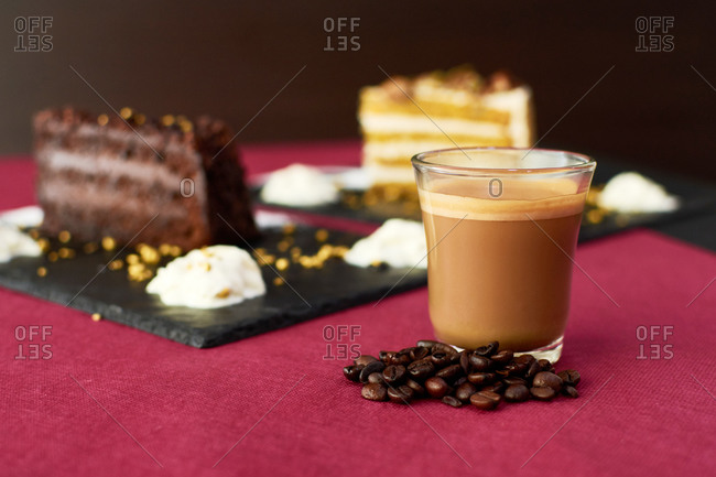 Glass cup of hot latte with coffee beans placed on table near pieces of cakes