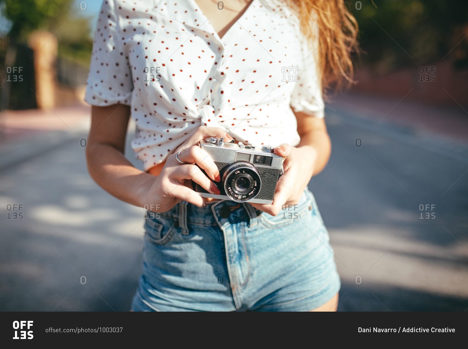 Crop view of anonymous young woman in casual wear holding photo camera in sunlight outdoors