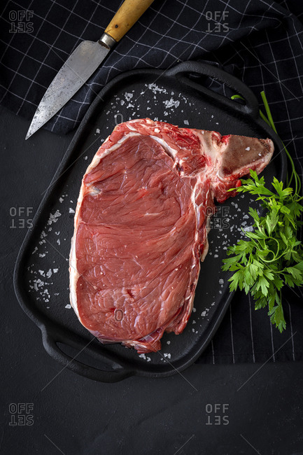 Fresh raw T-bone beef steak with red pepper, tomato, pink pepper and parsley ready to cook from above. Flat lay. Top view