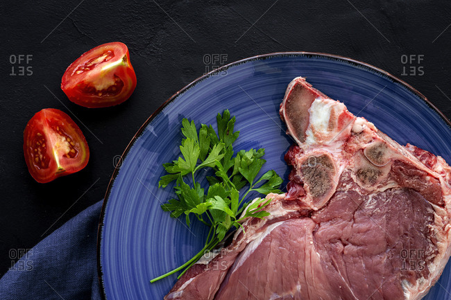 Fresh raw T-bone beef steak with red pepper, tomato, pink pepper and parsley ready to cook from above. Flat lay. Top view
