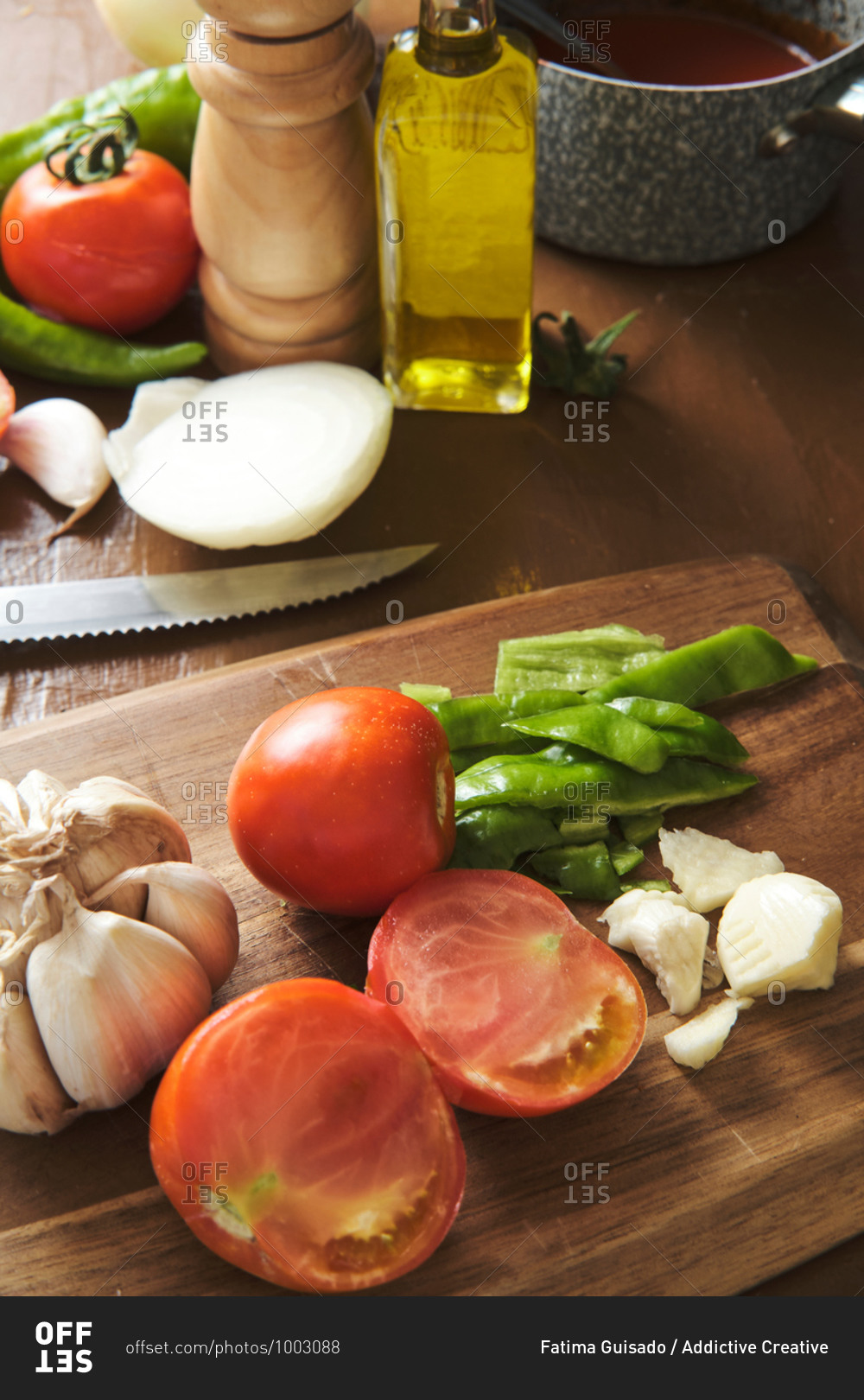 Chopped green pepper with garlic and tomatoes on cutting board placed on table with ingredients during preparation of Bolognese sauce