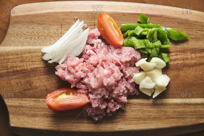 Top view of wooden cutting board with raw minced meat and chopped vegetables during preparation of traditional Italian Bolognese pasta