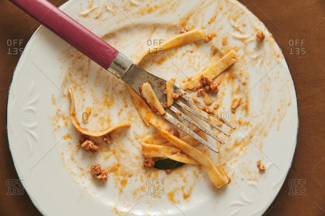 Top view of empty white plate and fork smeared with food after eating delicious Bolognese pasta