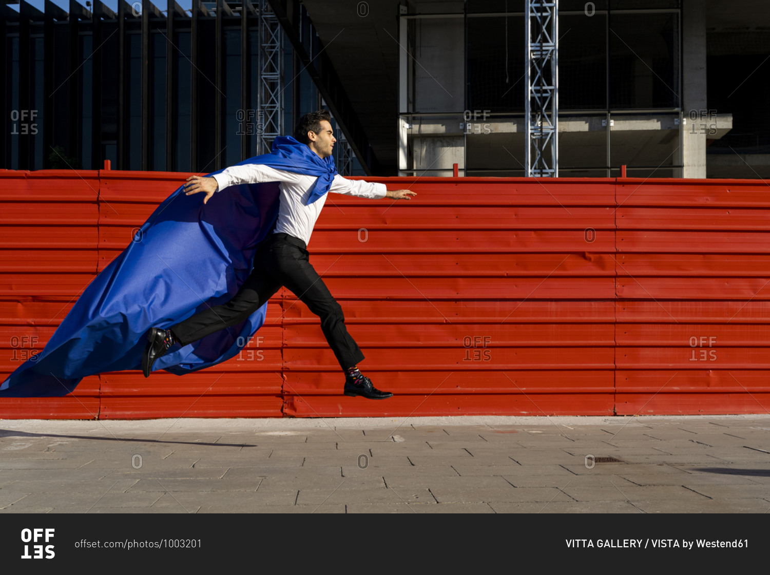 Businessman wearing superhero cape jumping on pavement in the city