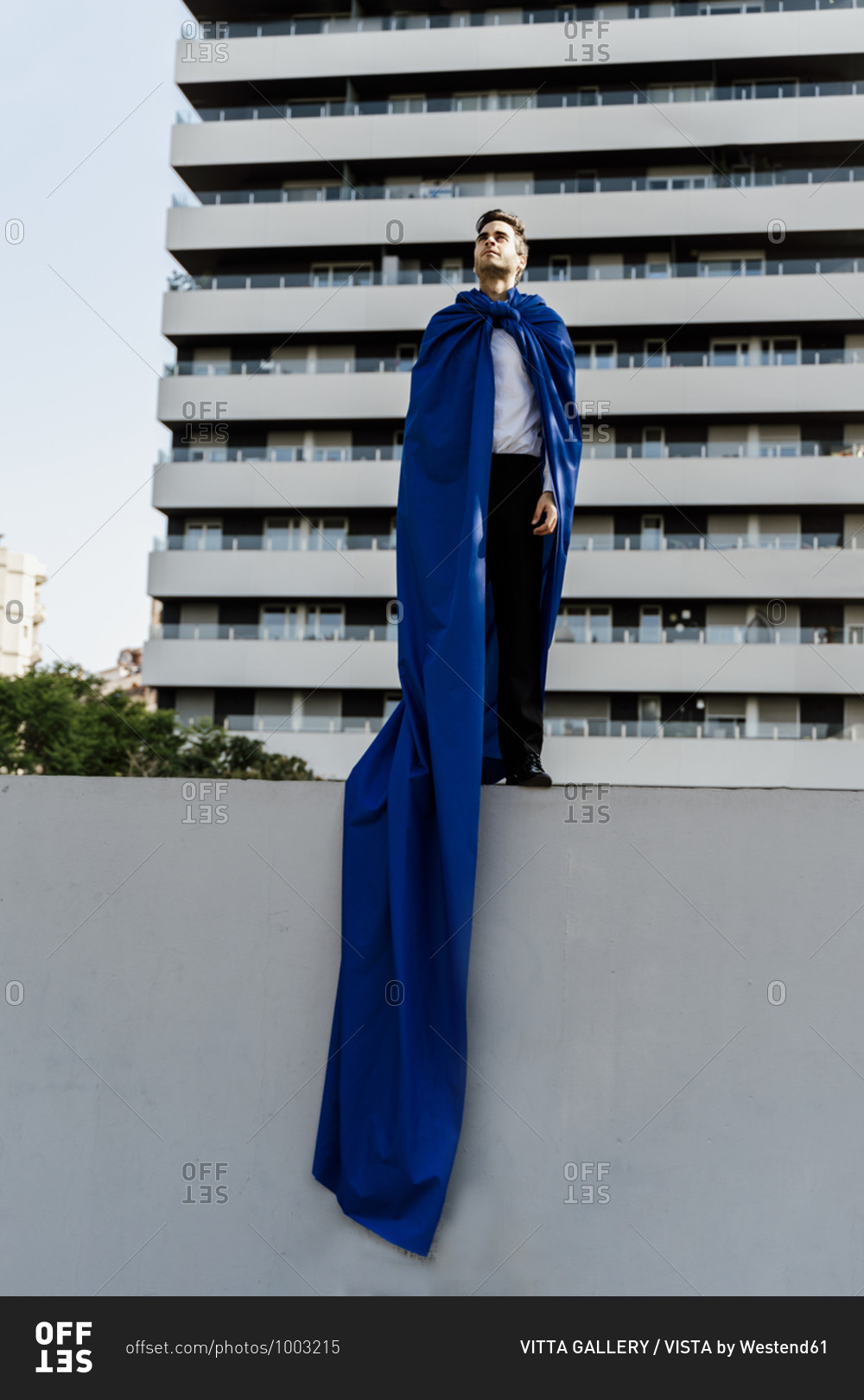 Businessman wearing superhero cape standing on a wall in the city
