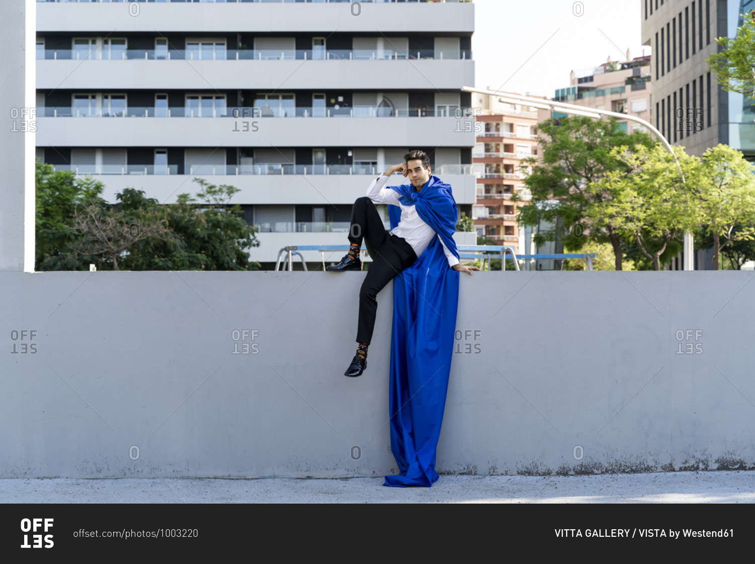 Businessman wearing superhero cape sitting on a wall in the city