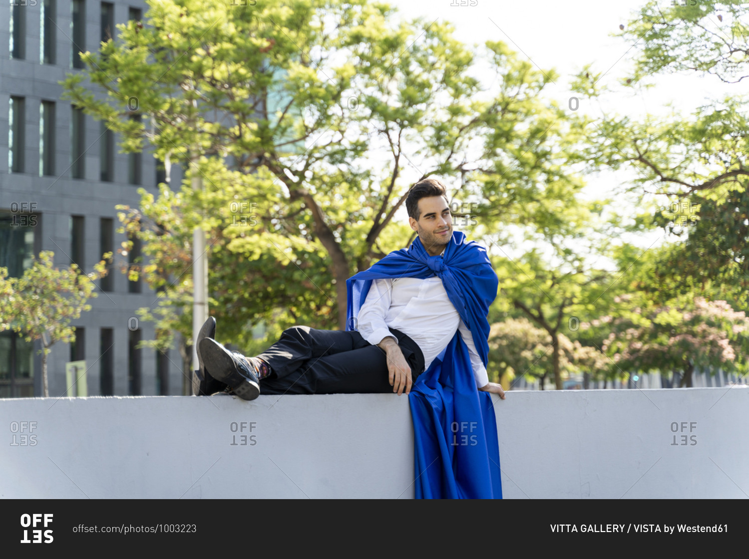 Businessman wearing superhero cape sitting on a wall in the city