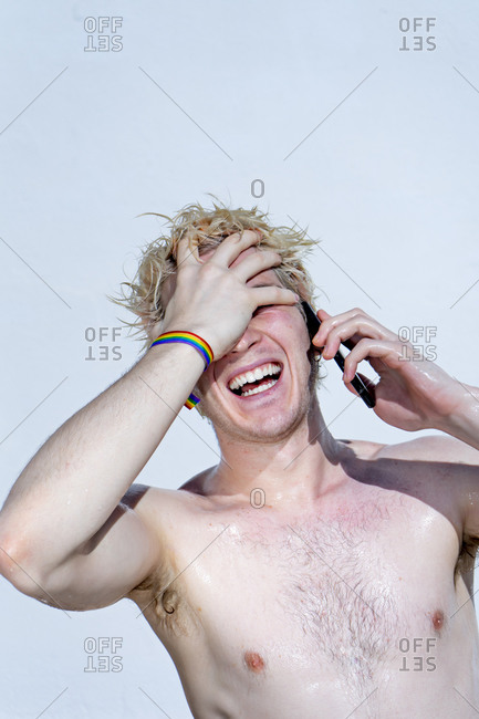 Attractive guy laughing with gay pride bracelet using smart phone