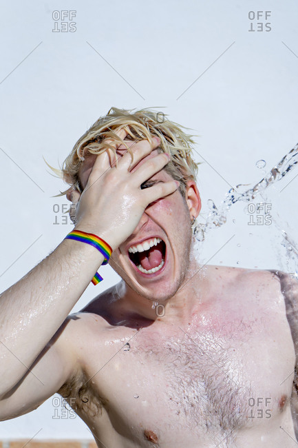 Attractive guy laughing with gay pride bracelet- hand on face