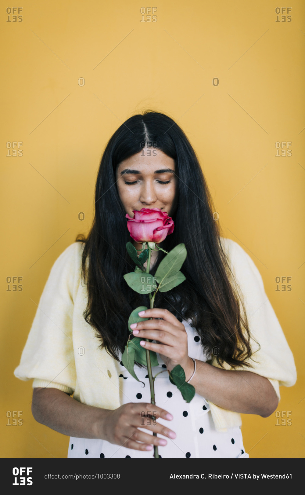 Young woman in front of yellow wall smelling rose