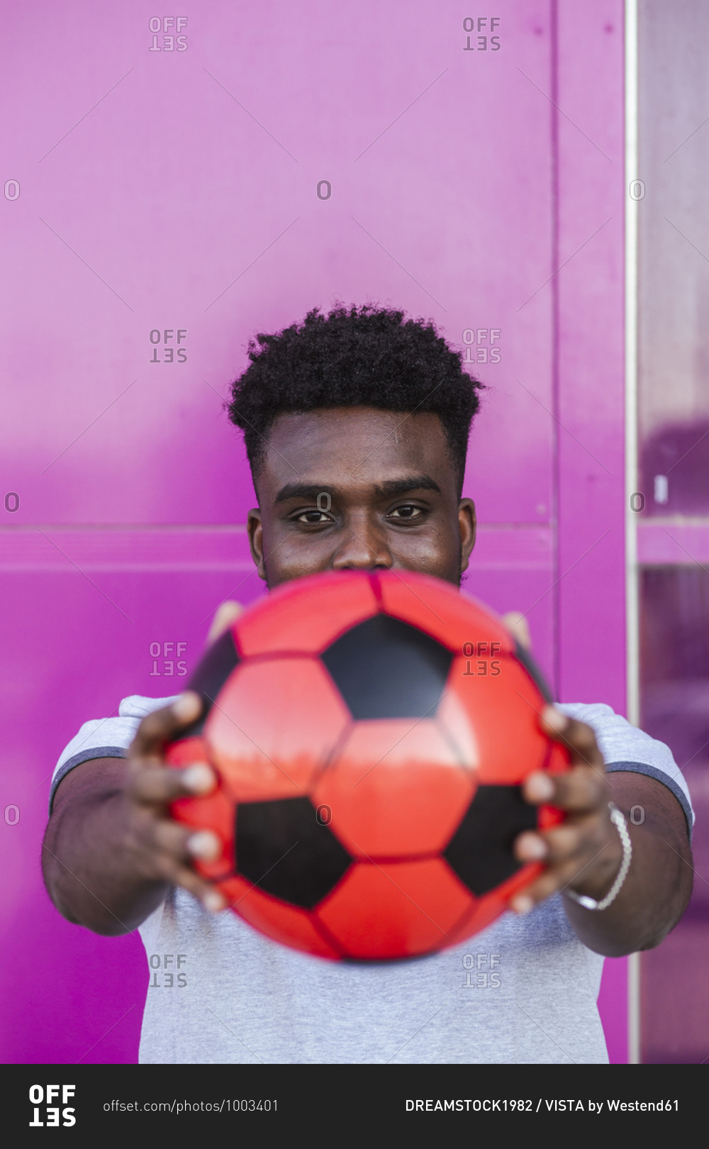 Close-up of young man holding soccer ball against pink color