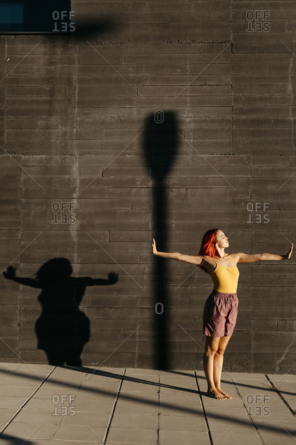 Dancing young woman casting shade on black wall at sunset