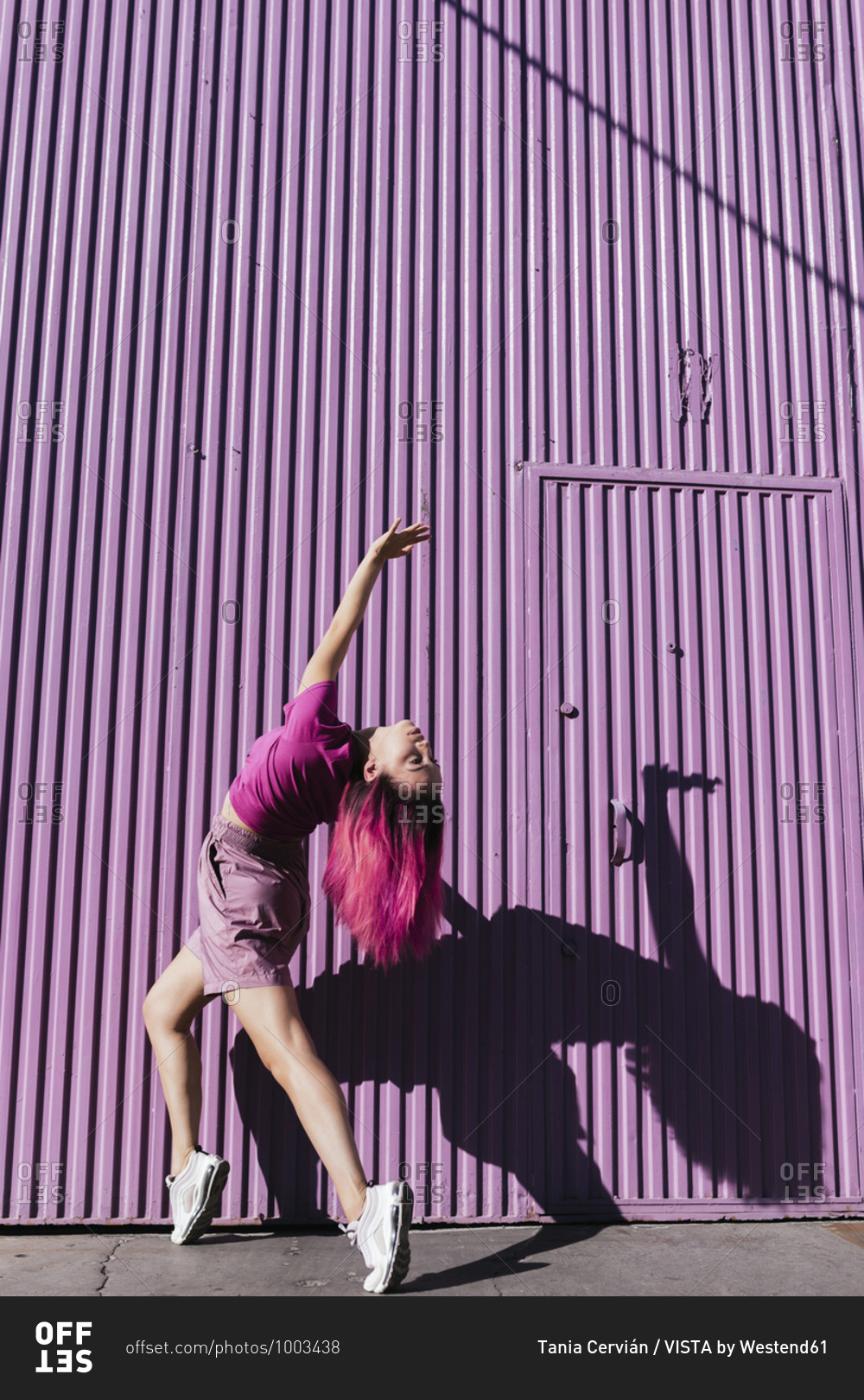 Young woman with dyed red hair dancing in front of purple wall in the city