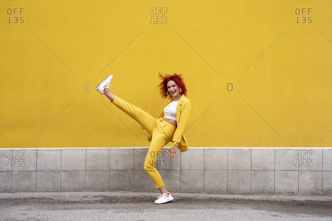 Energetic young woman in yellow suit running and jumping in front of yellow wall