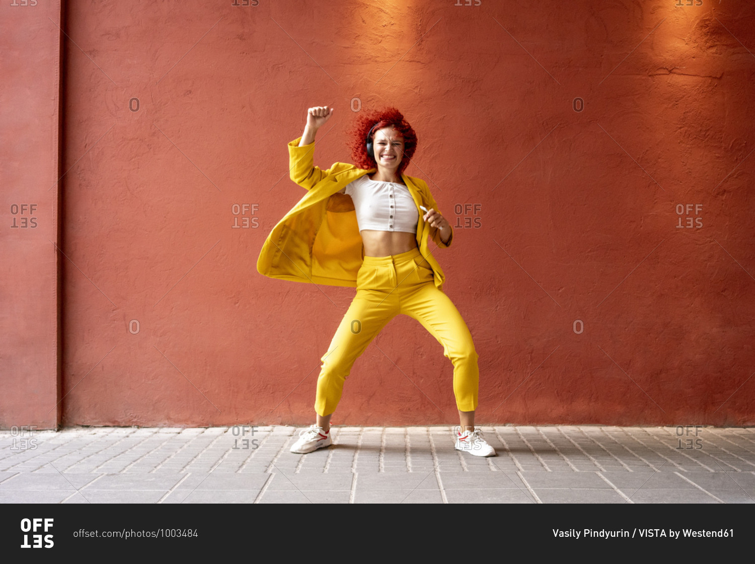 Young woman in yellow suit wearing headphones- dancing to music from her smartphone