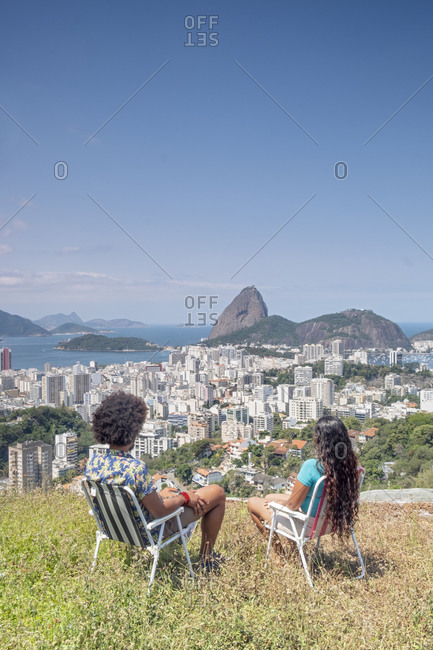 A multi-ethnic couple sitting together and looking out over Sugar Loaf mountain and the Rio skyline, Rio de Janeiro, Brazil, South America