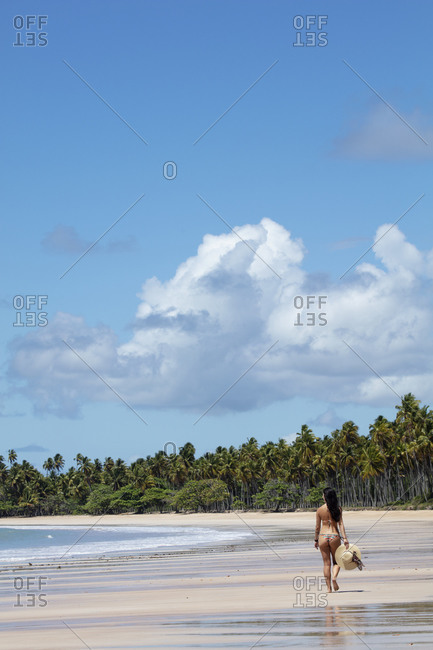 A beautiful, athletic Hispanic (Latin) woman in a bikini with a sun hat on a deserted tropical beach with back to camera, Brazil, South America