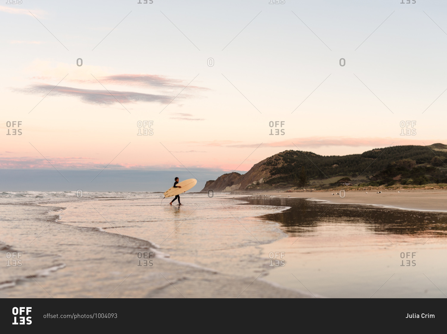 Boy carrying a surfboard at sundown on the coast of New Zealand