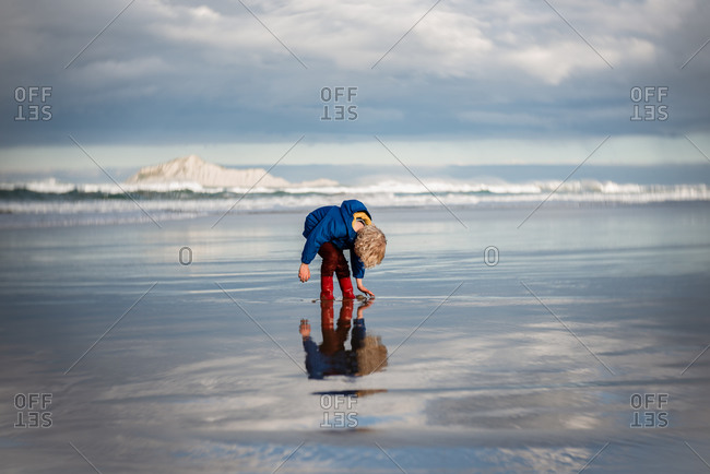 Young boy reaching down to touch sand and water on beach