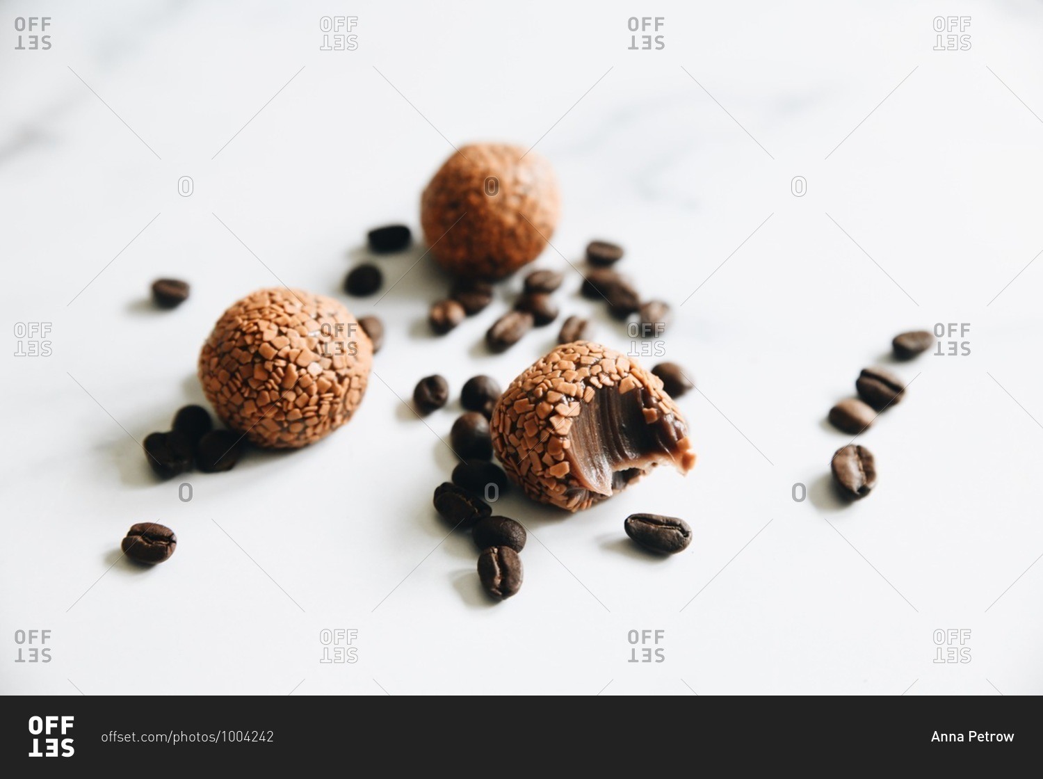Cappuccino brigadeiros missing a bite on white surface with coffee beans