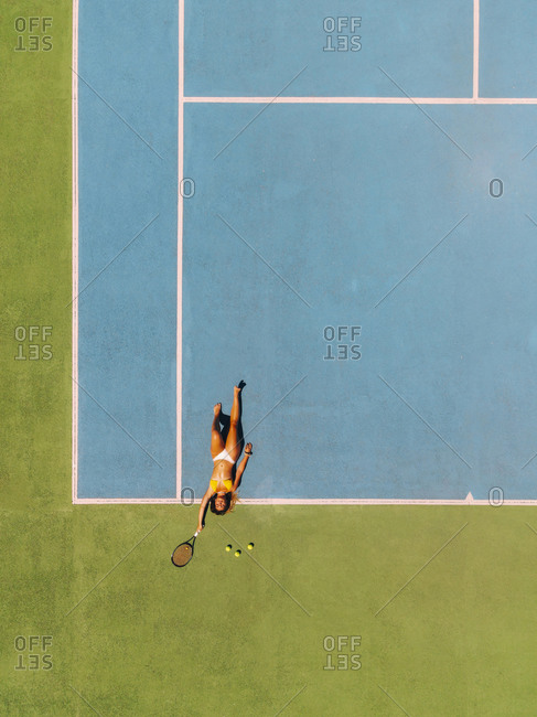 Blond woman lying on a tennis court with a tennis racket sunbathing
